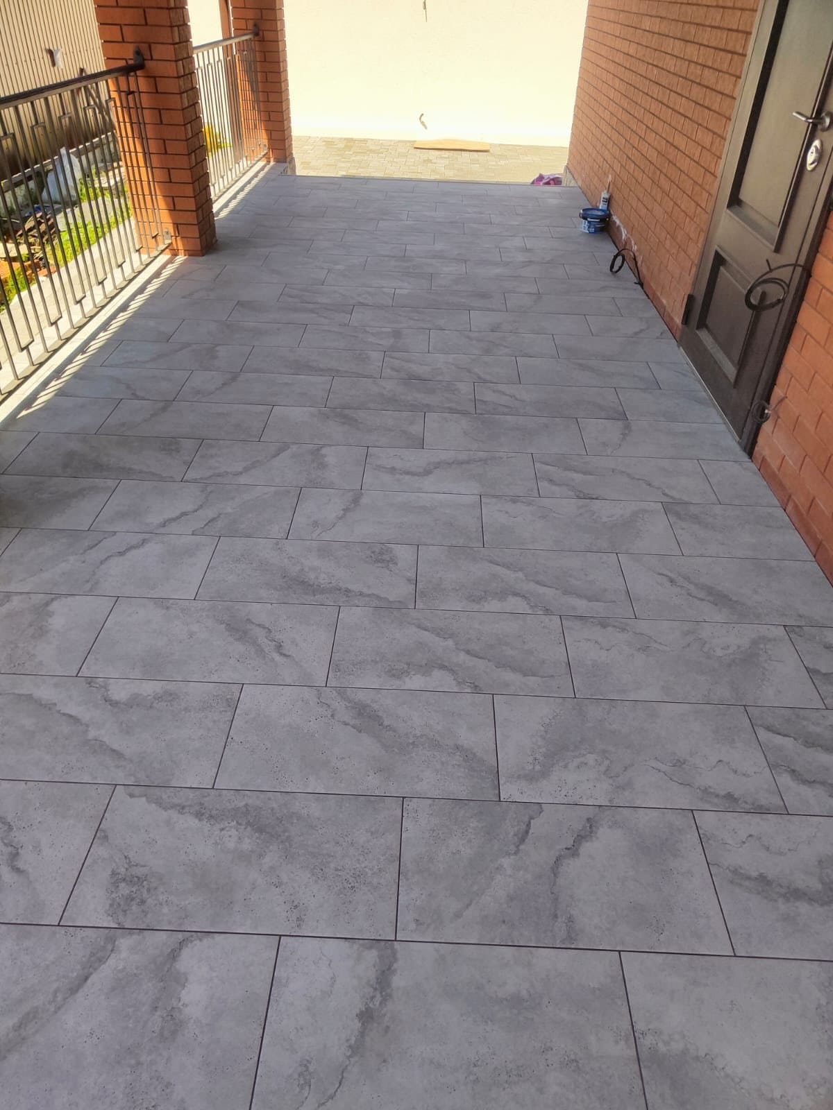 Nieuw terras met grote grijze tegels in marmerlook langs een bakstenen gevel