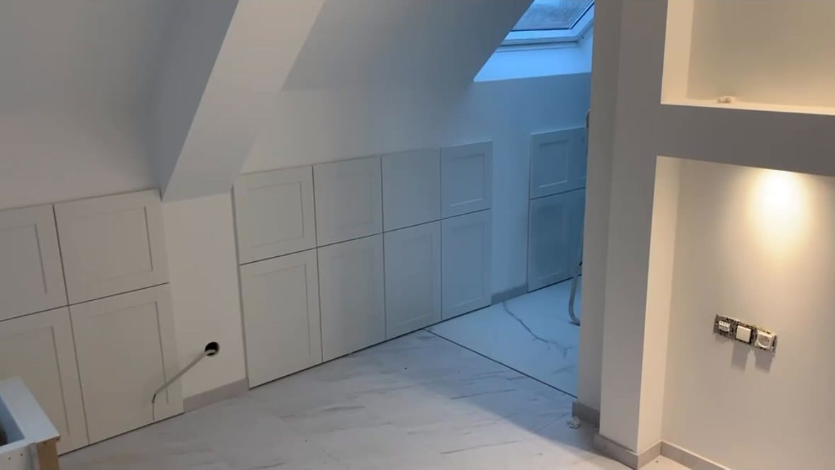 Zolder afgewerkt met witte inbouwkasten en een lichte marmerlook-tegelvloer